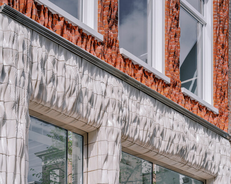 Textured building facade with a combination of red and white tiles and large windows reflects modern architectural design.