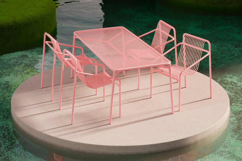 Pink wireframe table and chairs set on a circular concrete platform surrounded by water.