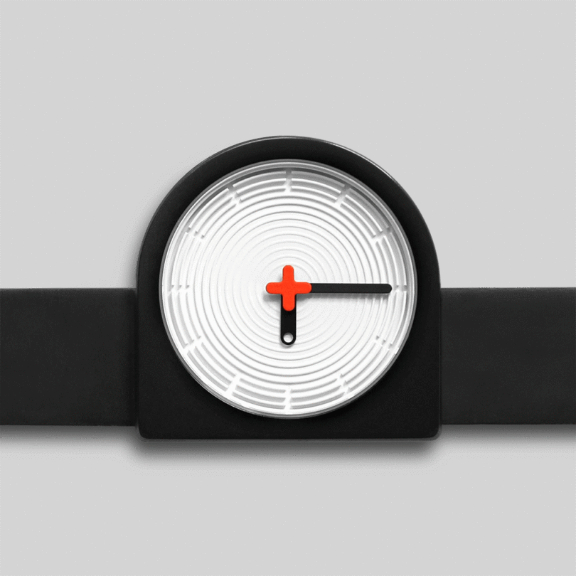 A modern clock with a circular white face, ridged texture, and minimalist black and orange hands, set against a rectangular black frame on a gray background.