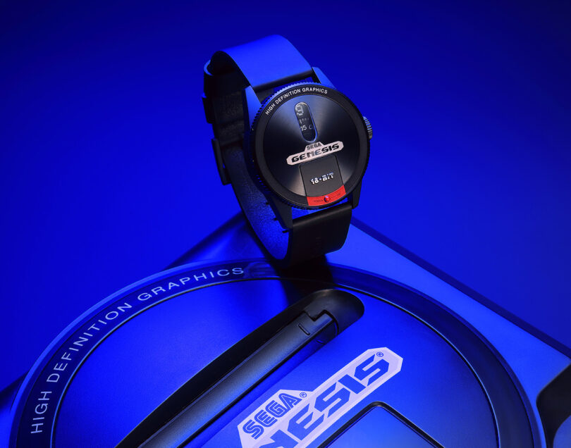 Montre-bracelet conçue pour ressembler à une console Sega Genesis posée sur la console elle-même, sous un éclairage bleu.