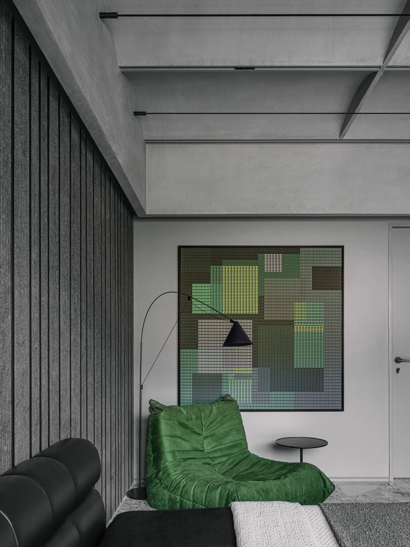 Modern living room with a green cushioned chair, black corner floor lamp, abstract geometric artwork on the wall, and a sleek black horizontal-paneled wall.