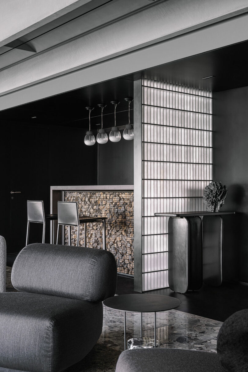 Modern interior with dark furniture, a textured bar with stools, hanging glasses, and a grid-patterned wall.