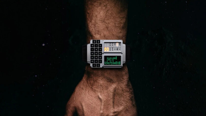 A hand wearing a digital wristwatch with a keypad and multiple buttons, set against a dark background.