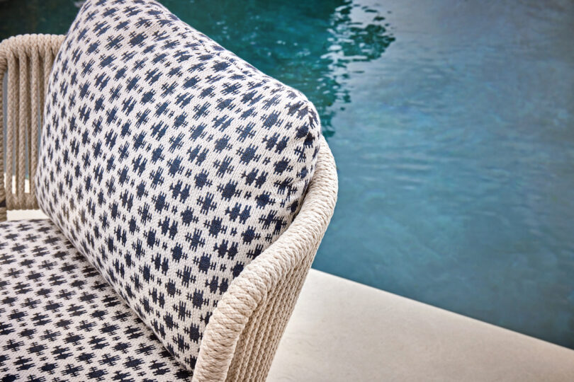 Outdoor chair with woven rope texture and black-and-white patterned cushions by a blue swimming pool