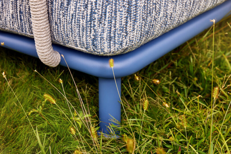 Close-up of a blue sofa leg on green grass with a textured fabric and a rope detail