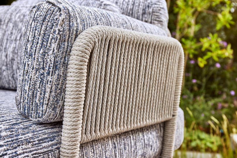 Close-up of an outdoor chair with textured fabric and rope detailing on the armrest, set against a blurred green garden background