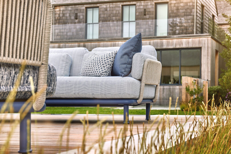 Outdoor patio with a light gray sofa, patterned throw pillows, and a modern wooden deck in front of a contemporary building