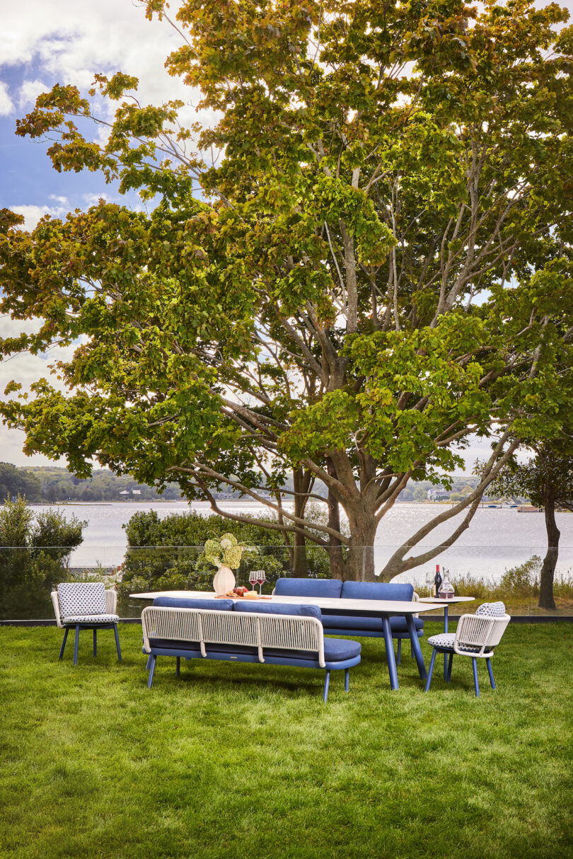 Outdoor seating on a grassy lawn with a large tree and a lake in the background