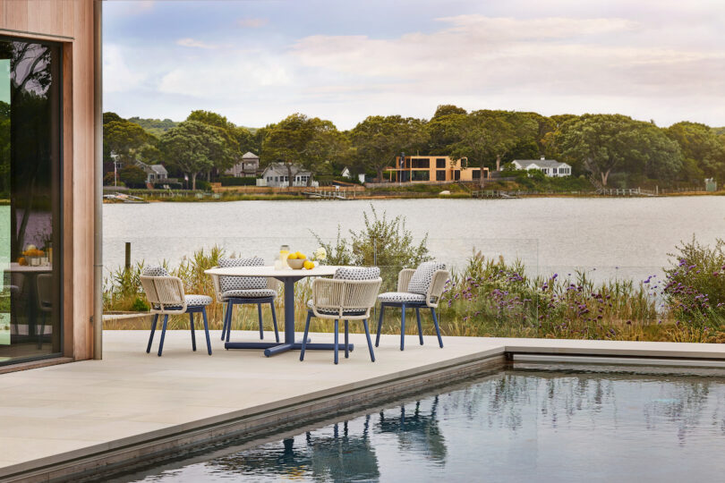 Outdoor patio with a table and chairs near a pool, overlooking a lake and trees in the background