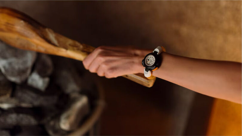 A person wearing a wristwatch is holding a wooden paddle near a stack of rocks.