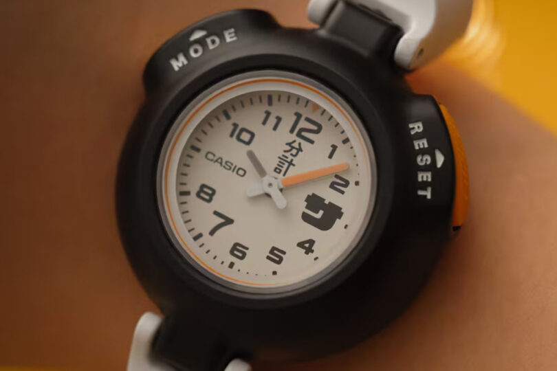 A black and white analog wristwatch with Arabic numerals, labeled "Casio," showing the time as 10:10. The watch features mode and reset buttons.