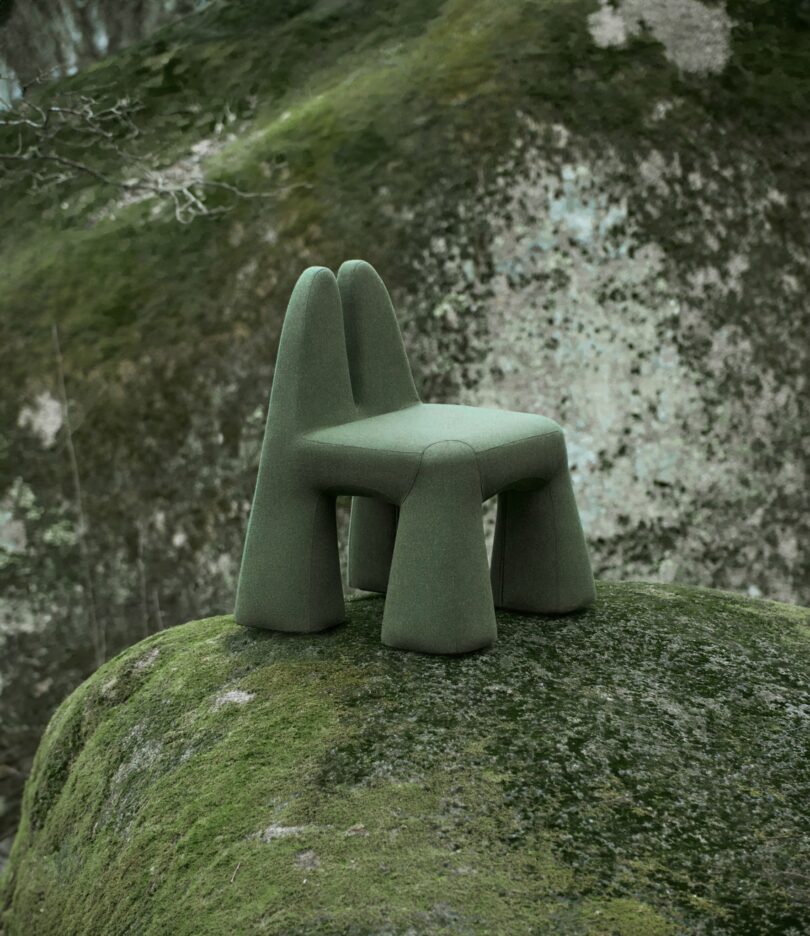 A uniquely shaped green chair with rounded legs sits on a moss-covered rock