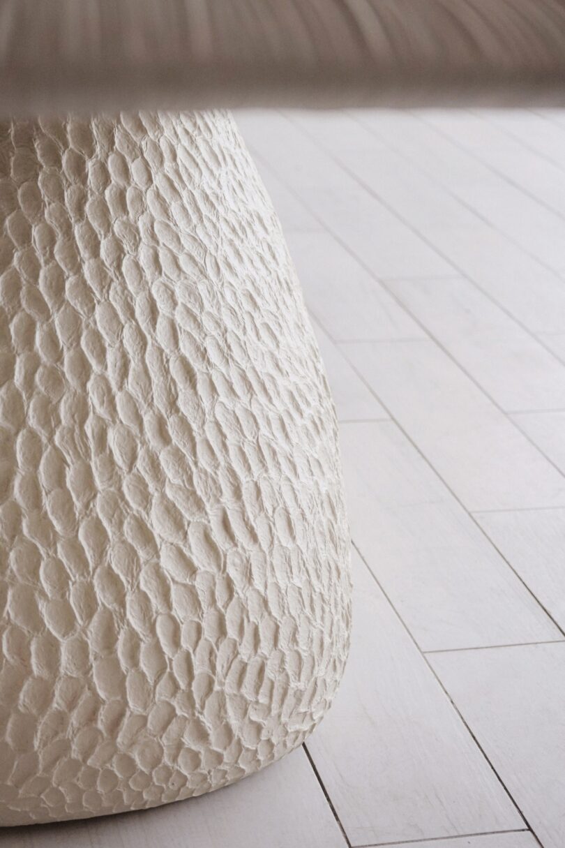 Close-up of a textured, white surface with a scale-like pattern, set against a light wood floor background