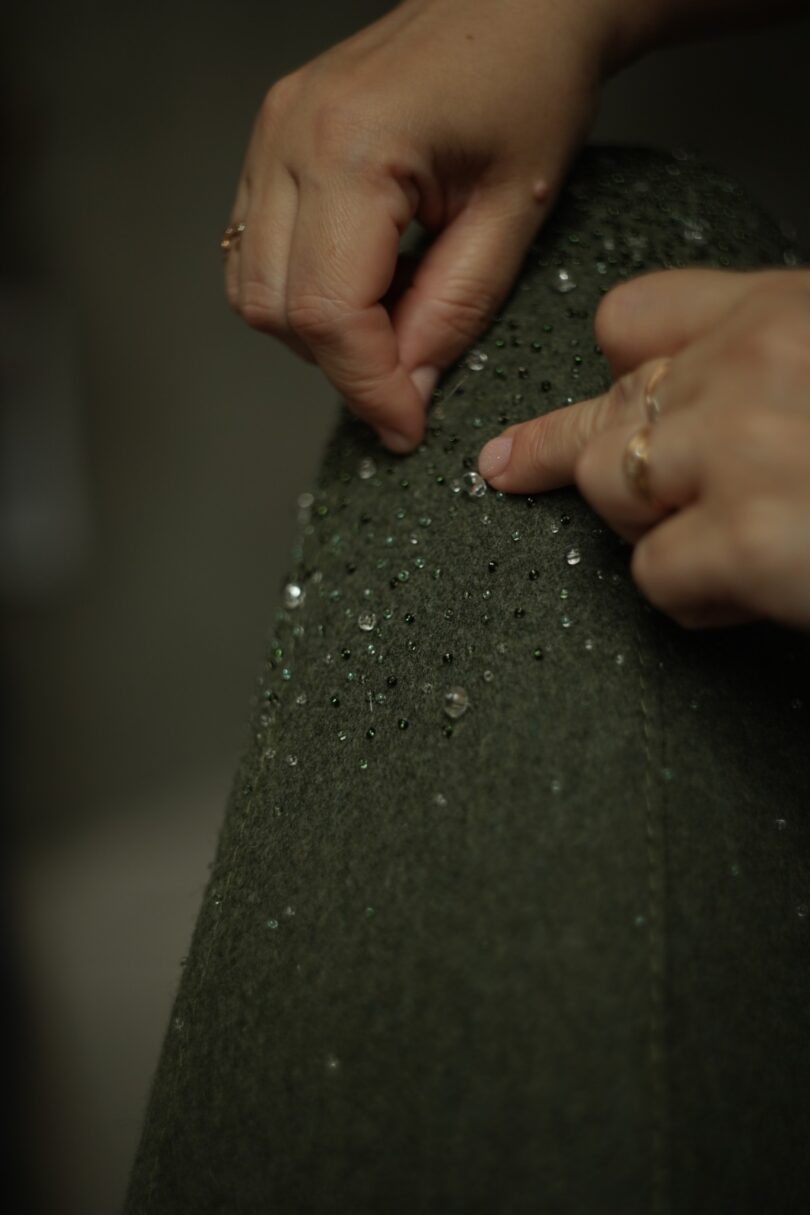 Hands attaching or adjusting sequins on a green fabric