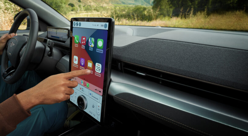 Person using a touchscreen in a car, displaying various apps and a calendar.