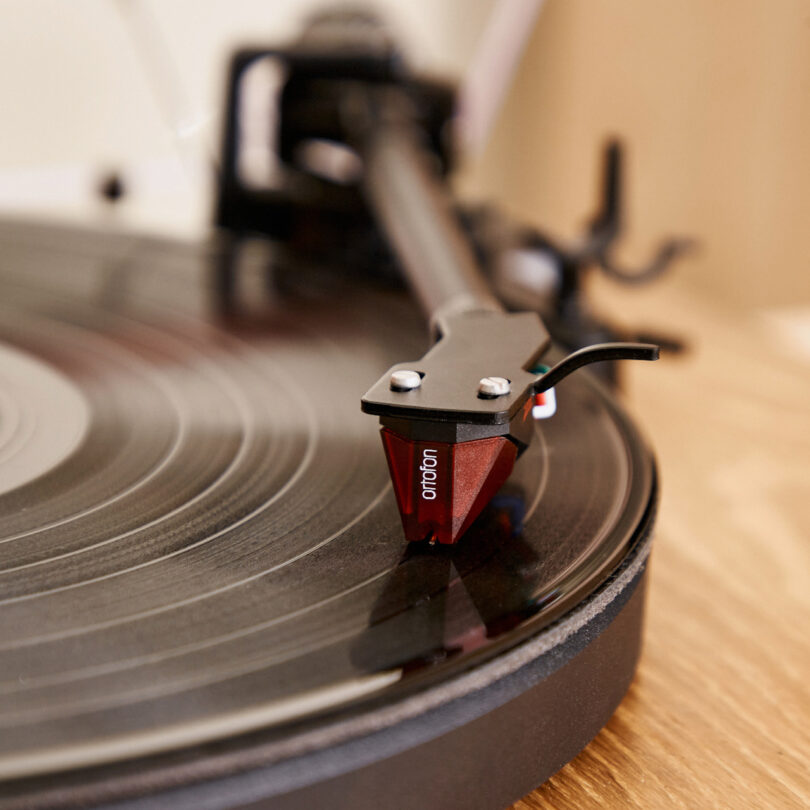 Close-up of a red tonearm and stylus on a vinyl record being played on a turntable.