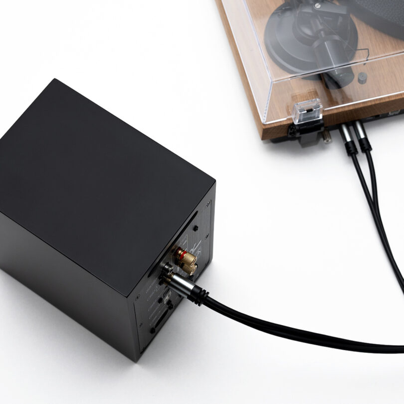 A black audio amplifier connected to a turntable with visible cables. The turntable has a wooden base and a clear dust cover.