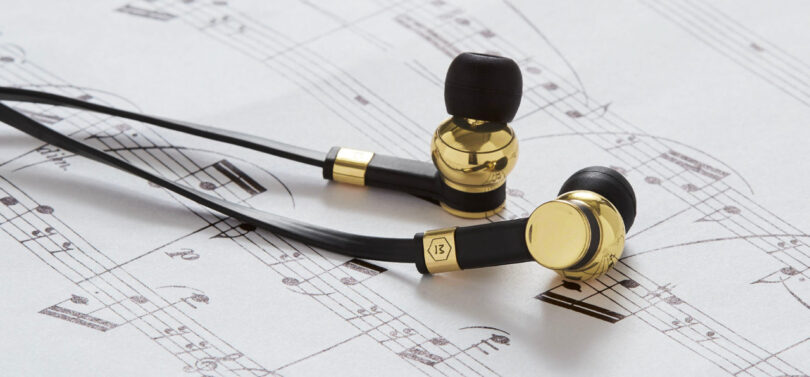 Gold and black earbuds rest on a sheet of music.