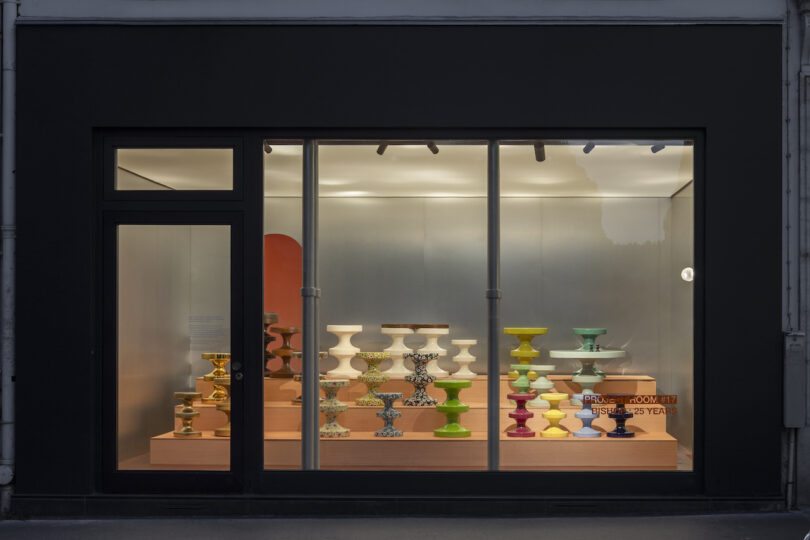 Storefront window display showcasing various colorful pedestal bowls arranged on tiered wooden platforms