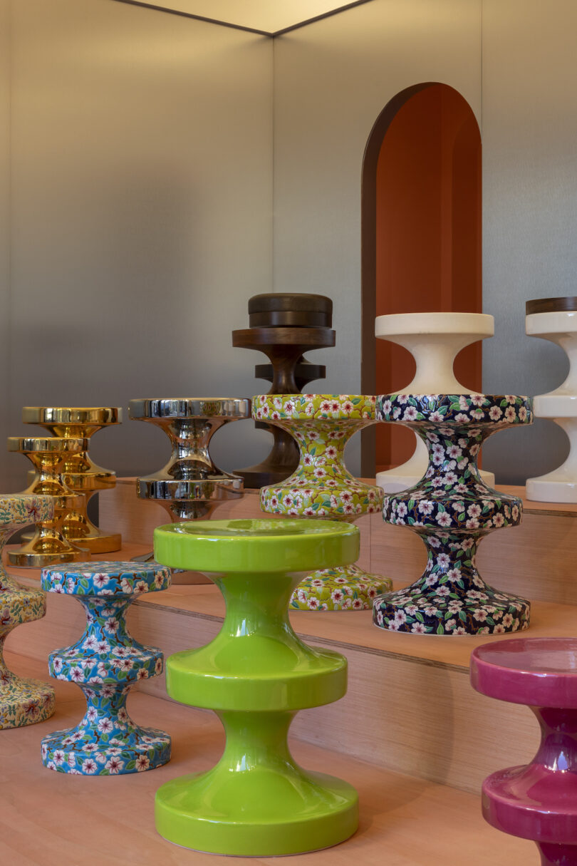 A display of colorful, uniquely shaped stools arranged on tiered wooden platforms