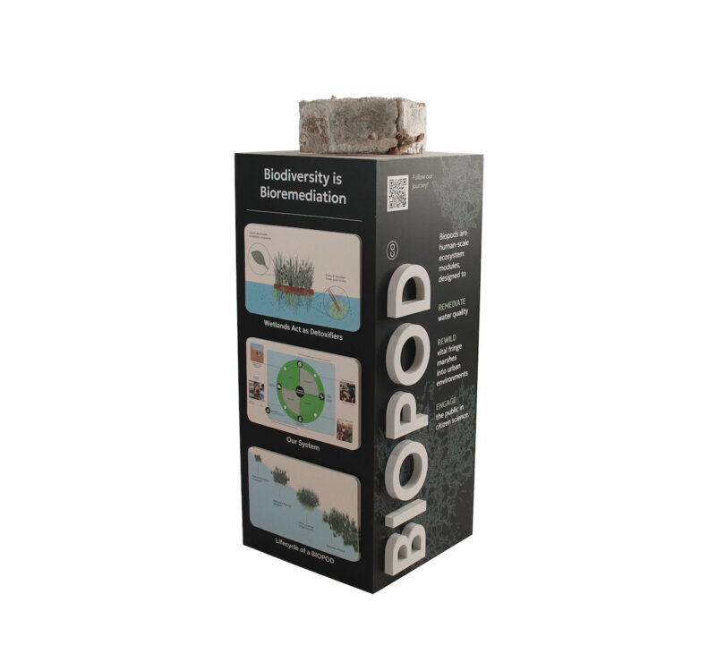 Tall black box labeled "BIOPOD" with images and text about biodiversity and bioremediation. A gray cylindrical item sits on top