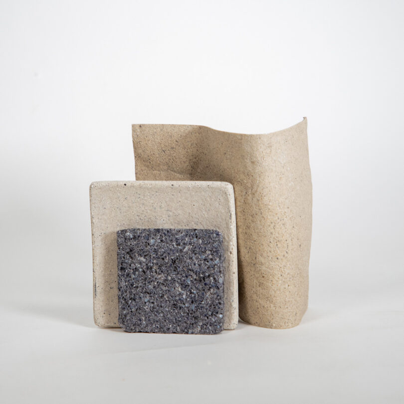 Three textured stones arranged artistically: a gray rectangular stone, a smooth beige curved stone, and a flat square stone with a rough surface