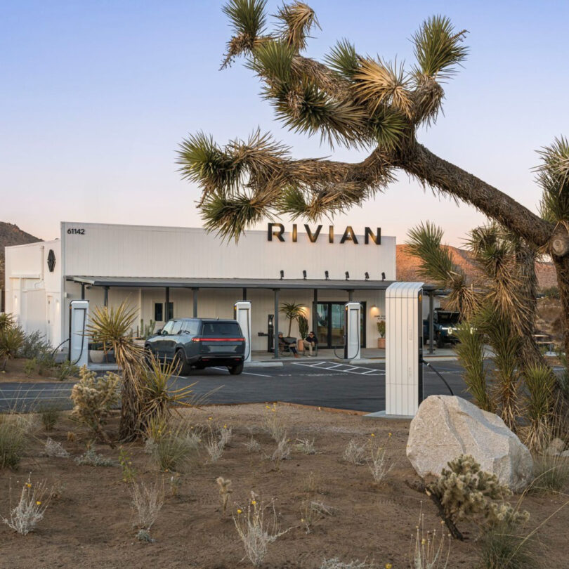 A Rivian charging station in a desert setting, with several chargers and a parked vehicle under a clear sky.