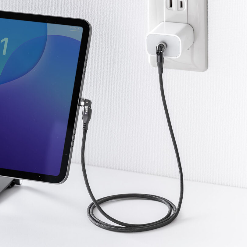 A tablet is connected to a power outlet with a braided charging cable.