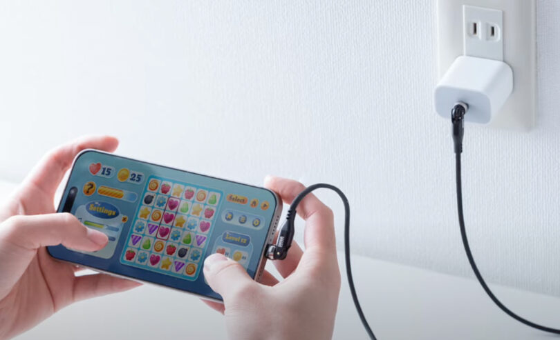 Person playing a matching puzzle game on a smartphone while it is charging from a wall outlet.