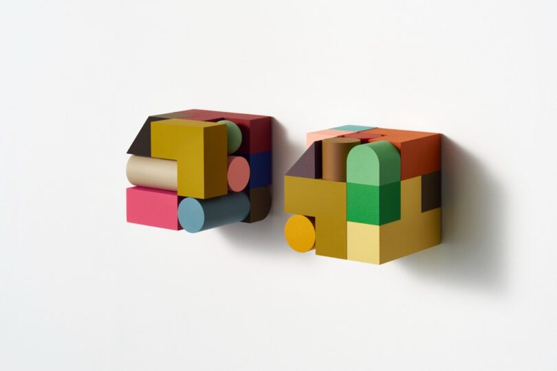 Two colorful, geometric 3D wall sculptures composed of various shapes in different colors, mounted on a white background