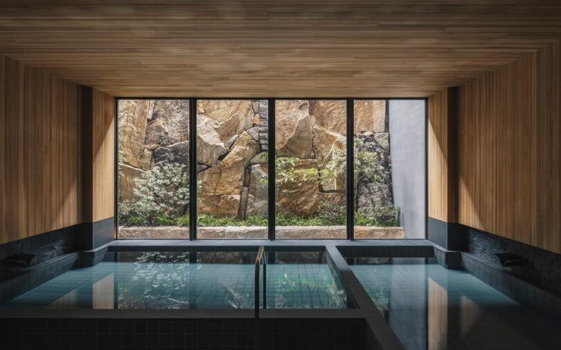 Indoor pool with wooden ceiling, large windows, and a view of a rock wall and greenery outside