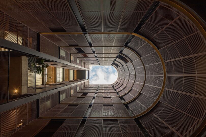 Upward view of a tall building's interior with an open skylight, showing a cloudy sky above