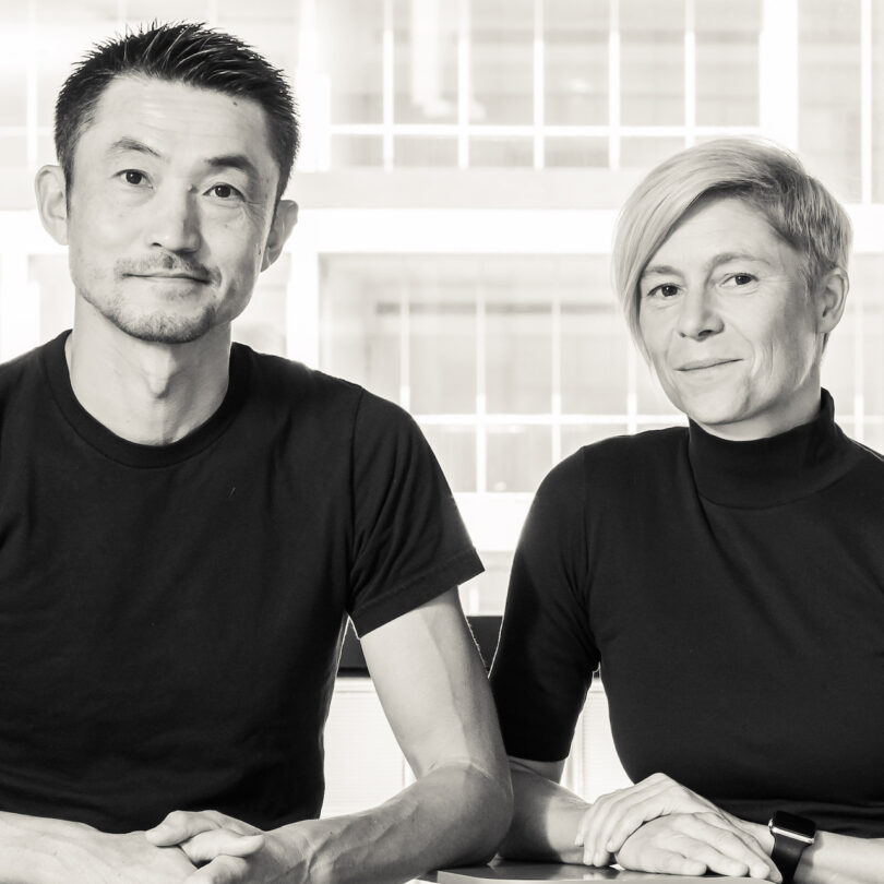 man and wonan, both in black shirts, are sitting together in front of a window.