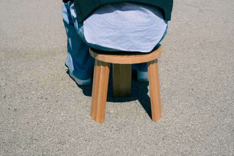 Person sitting on a small wooden stool on a paved surface