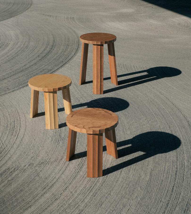 Three wooden stools of varying shades placed on a textured concrete surface with distinct shadows