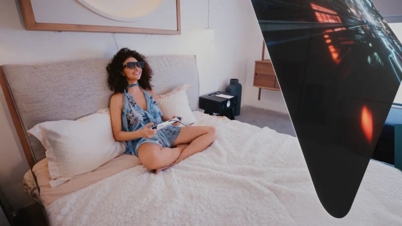 Woman in bed playing video games with the Xreal One smart glasses on.