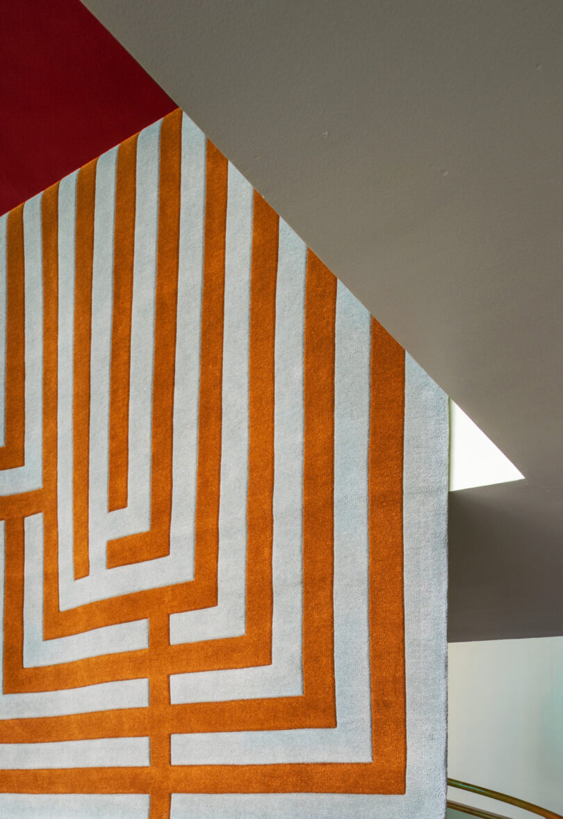 A geometric rug with orange and light blue lines drapes over a corner, reminiscent of the artistry found in LAYERED's timeless collections, against a ceiling with red and gray sections.