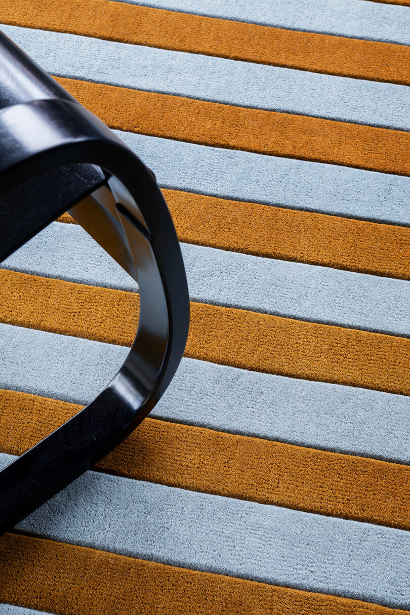 Close-up of a modern chair leg on a striped carpet with alternating orange and light blue stripes, crafted to perfection over 10 years.