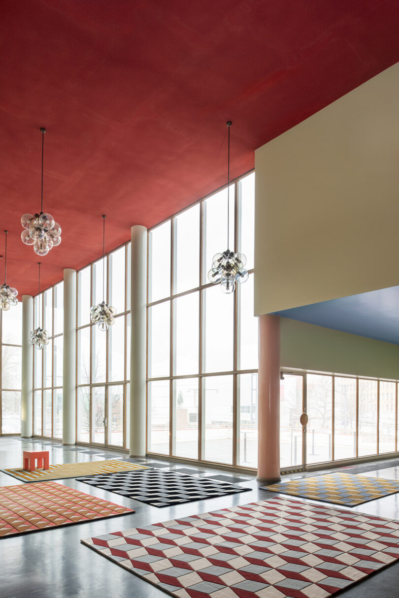 Spacious room with large windows, a red ceiling, and geometric patterned carpets from the 10 Years Unfolded LAYERED collection, complemented by modern pendant lights.