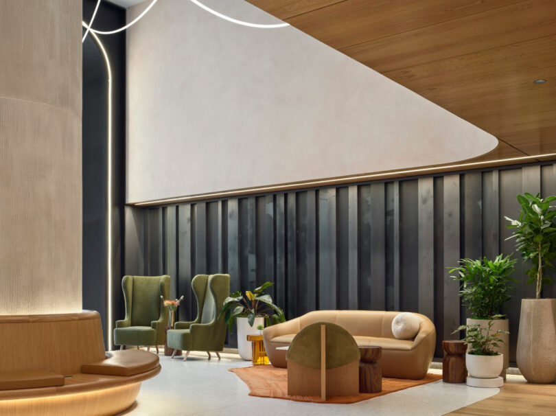 Modern lobby with green chairs, a beige sofa, wooden ceiling, decorative plants, and a large geometric wall design.