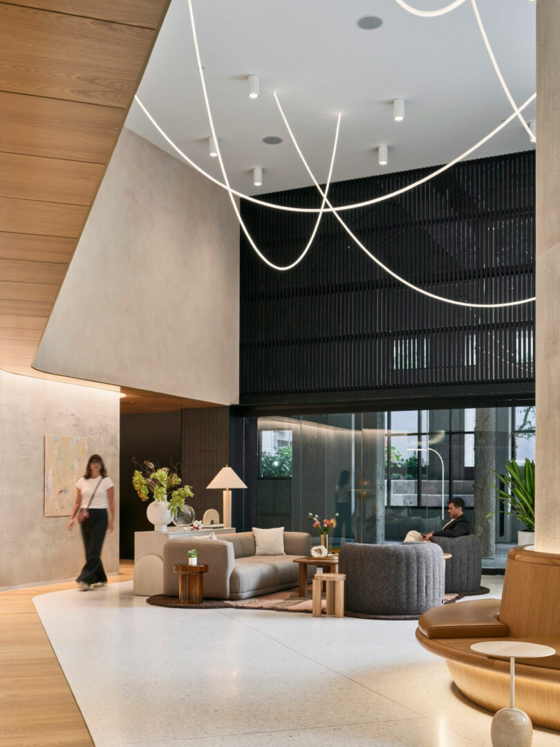 Modern lobby with high ceilings, unique lighting, and contemporary furniture. People are seated and walking.