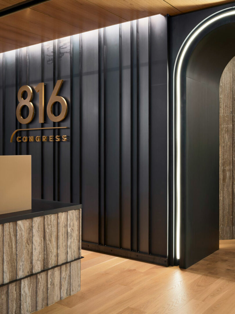 A modern lobby with a wood and metal design. The number "816" and the word "Congress" are displayed on the wall. A large, illuminated archway is present on the right.