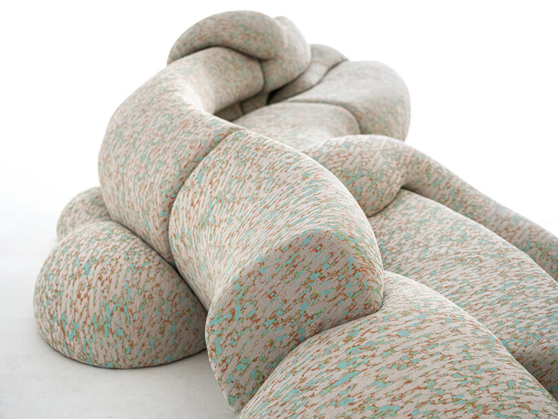 Abstract, curvy sofa with a textured, multicolored fabric pattern, displayed against a plain white background.