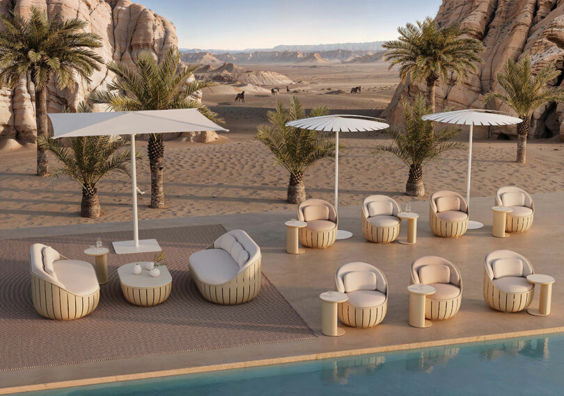 Outdoor seating area with modern furniture, umbrellas, and a pool in a desert setting with palm trees and rock formations in the background.