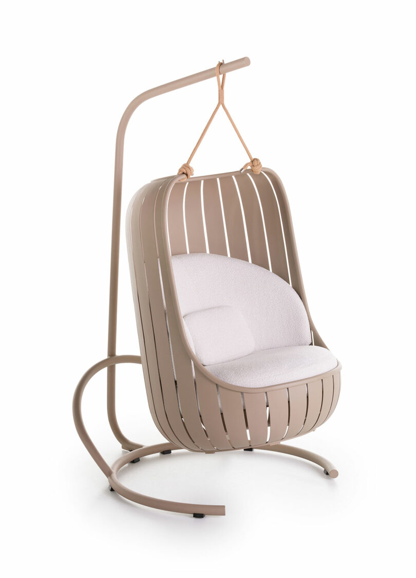 Modern hanging chair with a beige metal frame and cream cushion, supported by a curved stand.