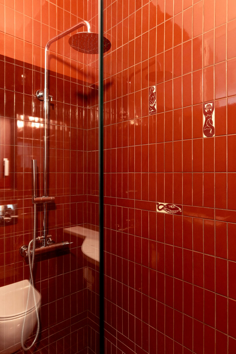 A shower with red tiled walls, a rainfall showerhead, and metal fixtures.