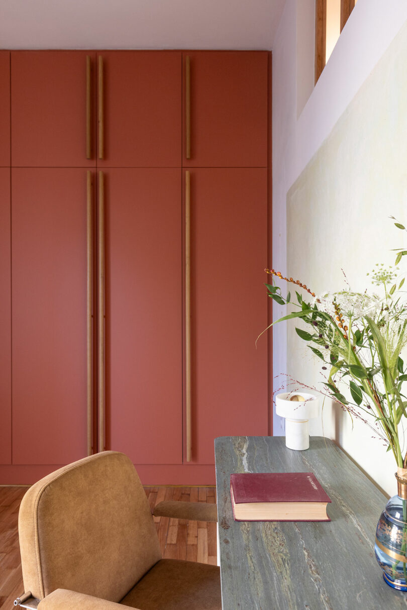 Room with red-orange cabinets, a green stone desk with a book and vase, and a brown chair.