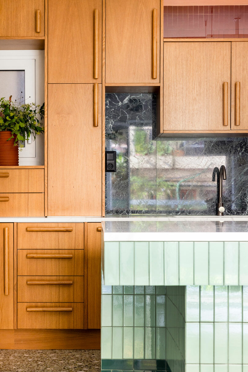 Modern kitchen with wooden cabinets, green tiled island, marble backsplash, and a potted plant near a small window.