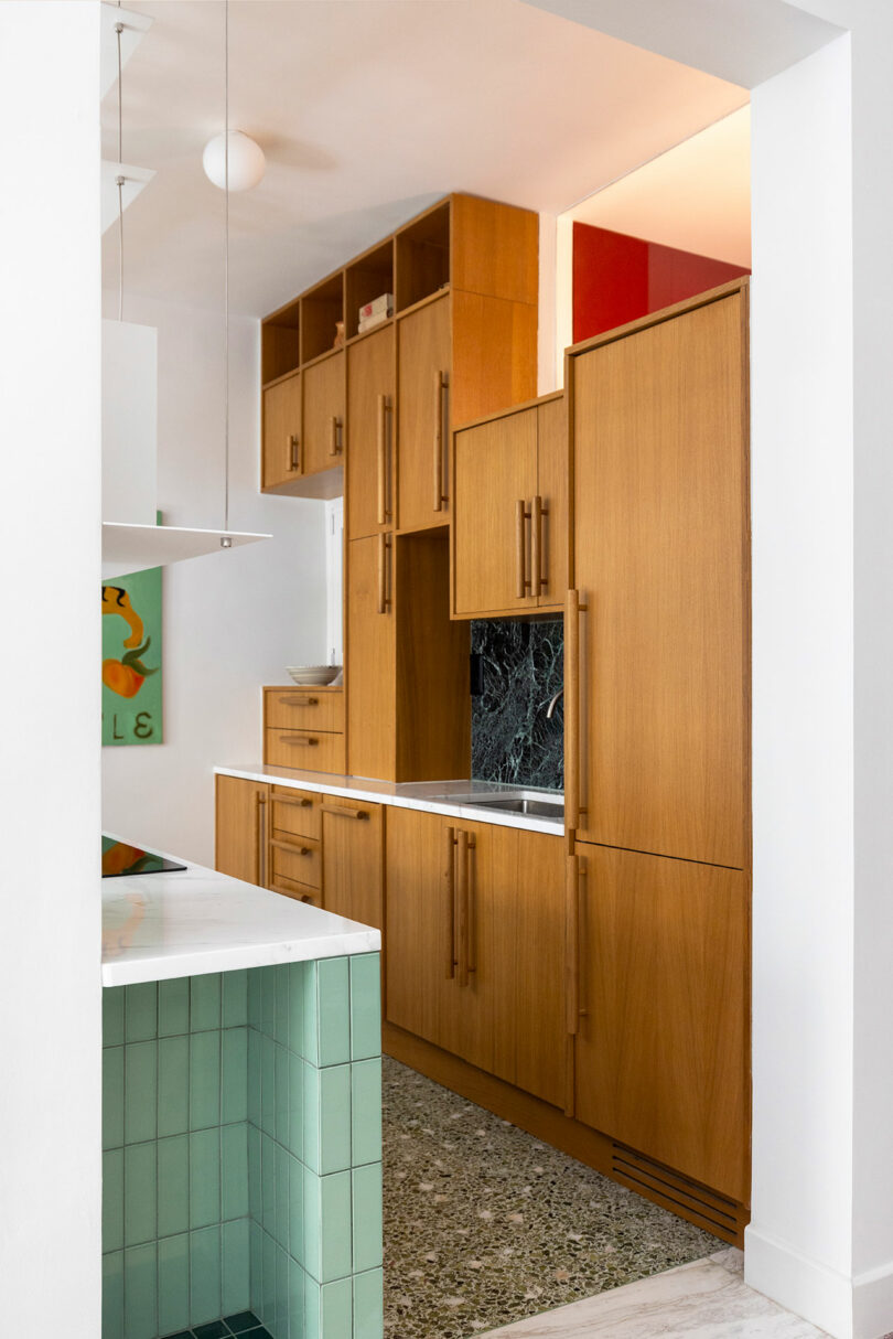 Modern kitchen with wood cabinets, marble backsplash, and green-tiled island. White walls and a spherical ceiling light accent the clean design.