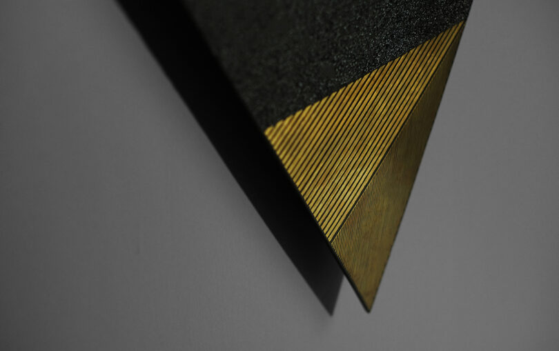 Close-up of a triangular artwork with textured dark and gold sections against a plain background.